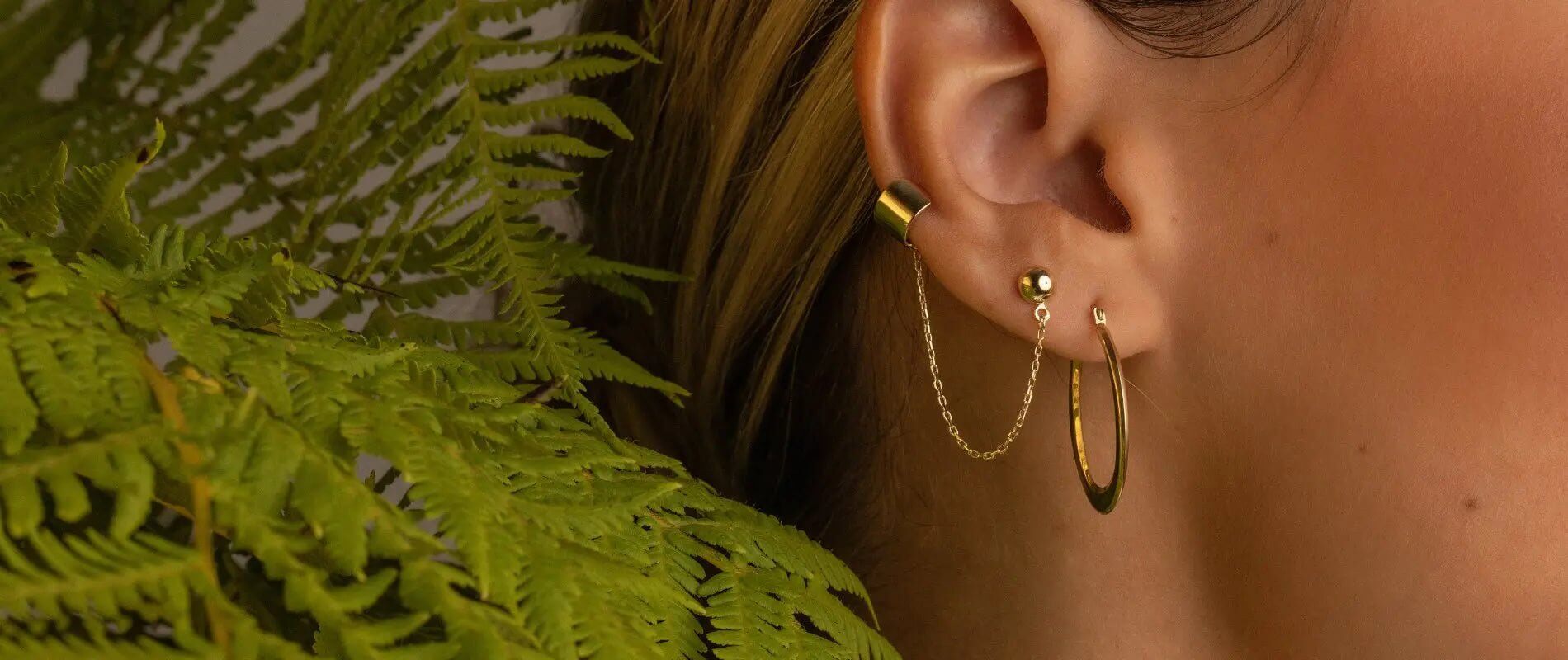 Stylish ear cuff displayed on a model, showcasing unique ear jewelry design with a fern backdrop.