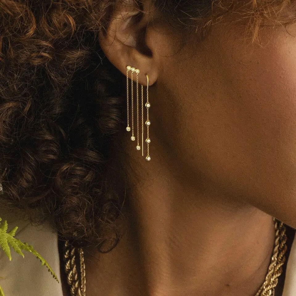 Diamond dangle earrings in 14k gold threader design worn by a model with curly hair.